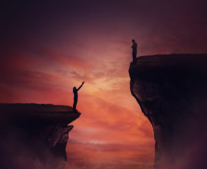 Image of two persons, one standing on a much higher peak looking down on the person on the lower point reach up. This is a concept image depicting inequality and social injustice.